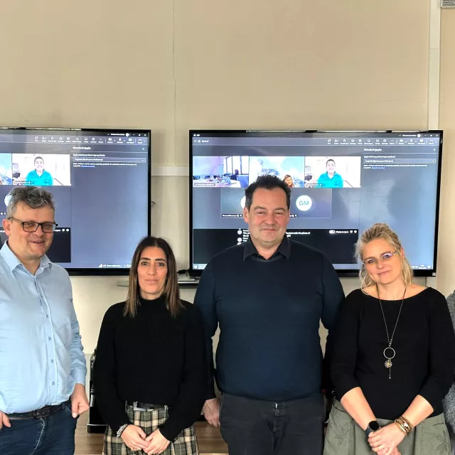 Pięcioro osób, dwóch mężczyzn i trzy kobiety, stoją na tle dużych monitorów powieszonych na ścianie