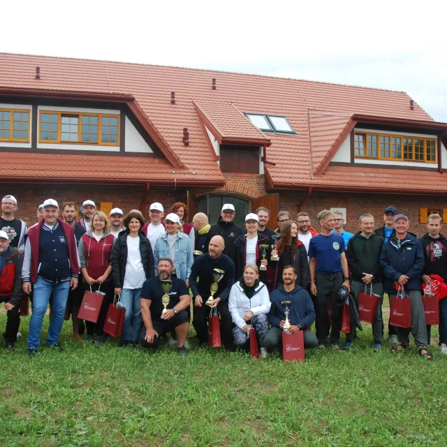 Liczna grupa osób stoi na na tle zrewitalizowanego budynku pietrowego z czerwonej cegły, z dwuspadowym dachem