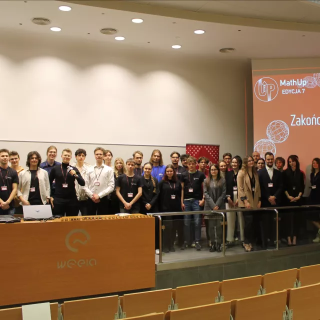 Grupa osób stoi w audytorium za katedrą, obok ekran z napisem Zakończenie konferencji