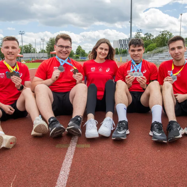 Pięciu sportowców z medalami siedzi na bieżni