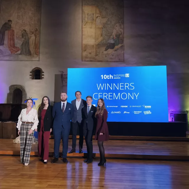 Sześcioro elegancko ubranych osób stoi w zabytkowym wnętrzu zamku, z tyłu ekran z napisem 10th winners ceremony