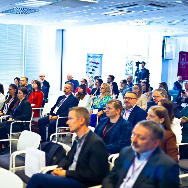 Mężczyzna przy mównicy przemawia do osób siedzących w sali konferencyjnej