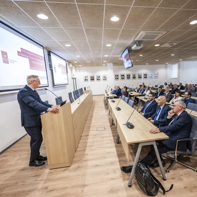 Uroczystość wręczenia stypendiów. Mężczyzna przemawia, stojąc za mównicą, liczna grupa osób siedzi w sali i słucha