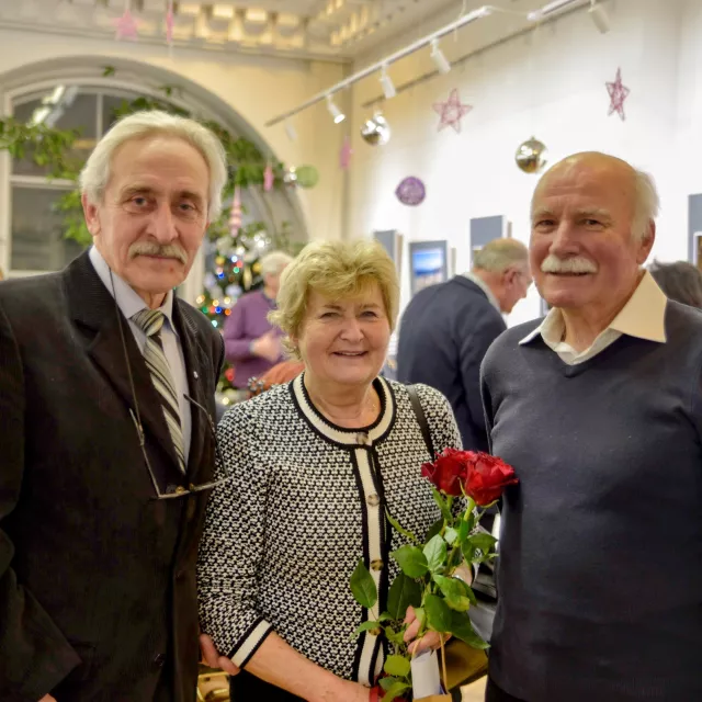 Trzy osoby, dwóch męższczyzn, a między nimi kobieta trzymająca różę