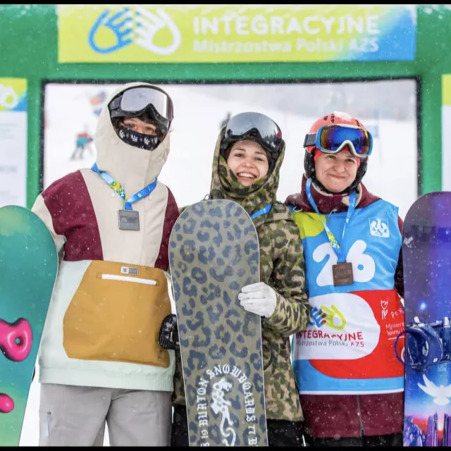 Trzy snowbordzistki z medalami na szyjach. Ubrane sportowo ze sprzętem w ręku.